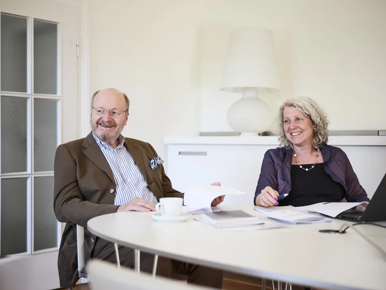 Ernst-Herbert Pfleiderer und Annett Baumeister am Schreibtisch im Gespräch miteinander
